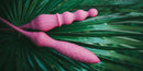 Adrien Lastic 2X double ended vibrator nestled on green palm leaves, showcasing its sleek design and vibrant pink color.