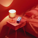 Biird Gii Glow Vibrator Mint on a bedside table with a lamp in a red-themed setting.