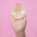 UVA Vanilla Non-Adhesive Round Nipple Covers held in hand against a pink background.
