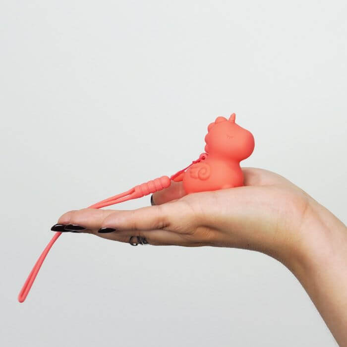 Hand holding Unihorn Mini Peachy Pony vibrator, pocket-sized and orange, showcasing its cute design and compact size.