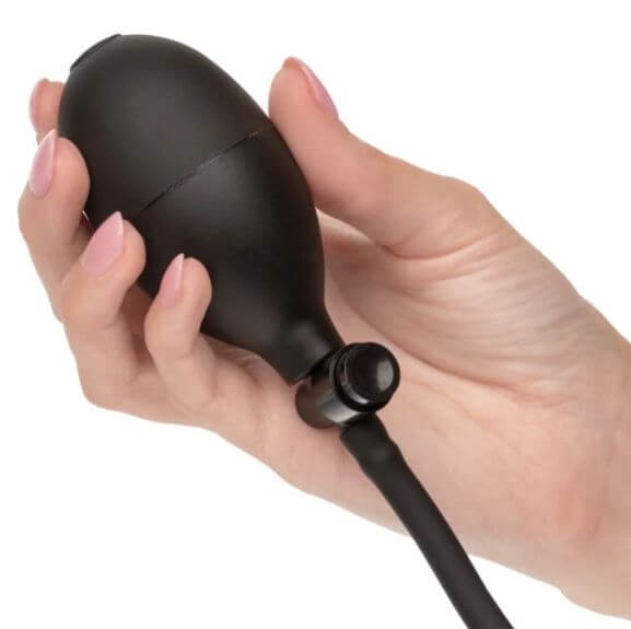Hand holding a black medical-ball hand pump for an expandable silicone inflatable plug used in anal play.
