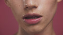 Close-up of a person's lips with a wet appearance against a pink background.