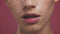 Close-up of a person's lips with a wet appearance against a pink background.