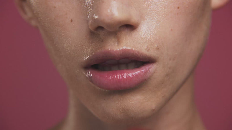 Close-up of a person's lips with a wet appearance against a pink background.