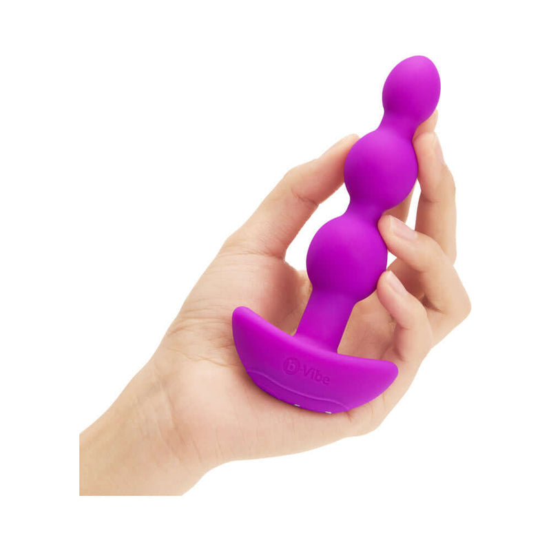 b-Vibe Triplet Remote Controlled Anal Beads Plug Fuchsia held in hand, showcasing its flexible design and tapered beads.