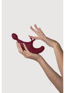 Fusion Red triple stimulation vibrator held in hand showcasing its ergonomic design and silky smooth texture.