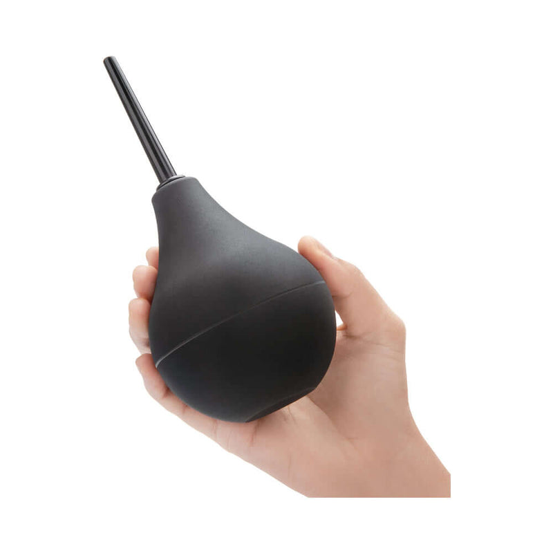 Person holding the b-vibe Classic Enema, a black cleansing tool designed for anal preparation.