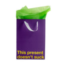This Present Doesn't Suck Color Gift Bag Purple with green tissue paper on top and a humorous message.
