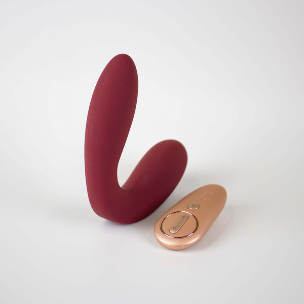 Hercules Remote C-Shape Vibrating Plug Wine Red next to its remote control for enhanced pleasure.