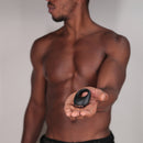 Je Joue Mio Rechargeable Vibrating Silicone Cock Ring Black held in hand by a shirtless man.