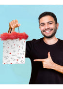 Smiling person holding Little Genie Dirty Stick Figures Gift Bag Red and White with red feather trim.