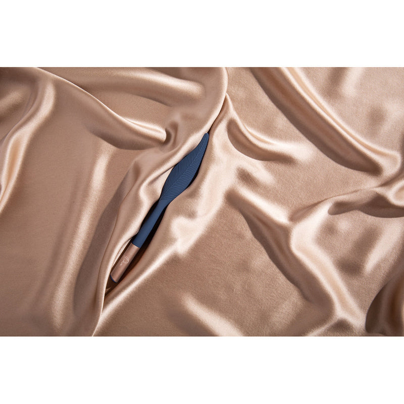 Deia The Feather Vibrating Tickler Silicone Blue nestled in luxurious satin fabric.