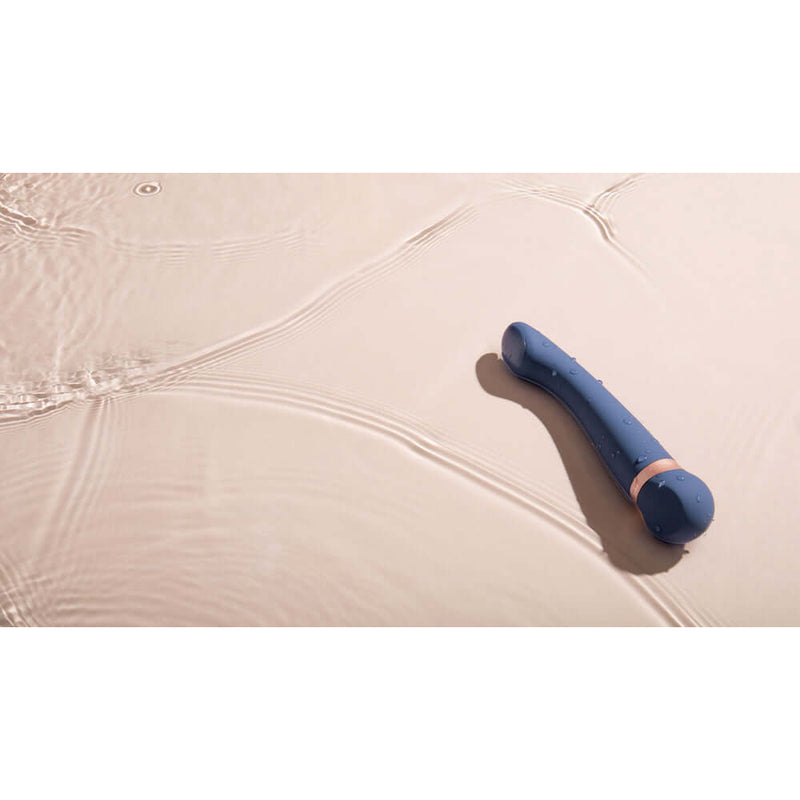 Deia The Hot Cold Temperature Changing G Spot Massager Blue on a smooth surface with gentle ripples around it.