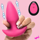 Bang Thrusting & Vibrating Silicone Butt Plug Pink in hand with remote control on a pink background.