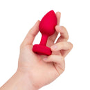 A hand holding the b-Vibe Vibrating Heart Anal Plug Medium Large Red, showcasing its heart shape and design.