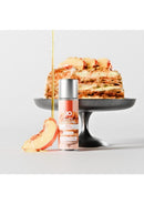 JO Bake Shoppe Lubricant Peach Cobbler 2 Oz next to a slice of peach cobbler on a black cake stand.