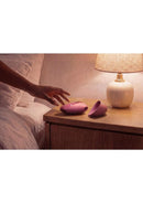 Womanizer Next Liberty Air Clitoral Stimulator Bordeaux on bedside table with a lamp and hand reaching for it.