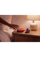 Womanizer Next Liberty Air Clitoral Stimulator Blue Red on bedside table with a hand reaching for it.
