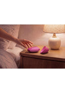Womanizer Next Liberty Air Clitoral Stimulator Pink on a bedside table next to a lamp, showcasing its compact design.