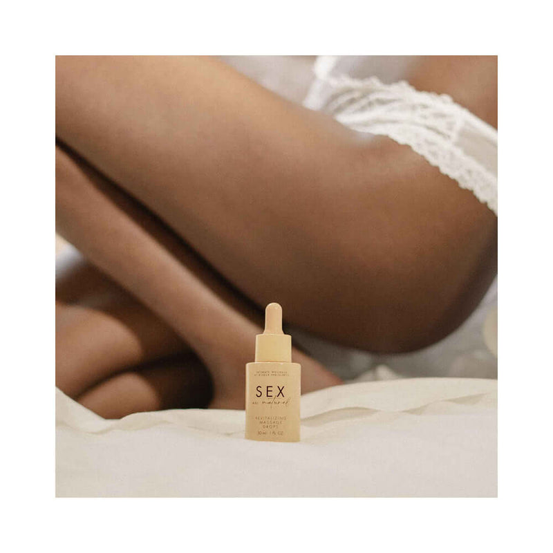 Bijoux Indiscrets Sex au Naturel Revitalizing Massage Drops 1 Oz bottle on a soft surface with a person's leg in the background.