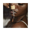 Bijoux Indiscrets Sex au Naturel Revitalizing Massage Drops 1 Oz in pipette held above shoulder