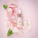 HighOnLove Mini Sensual Stimulating Oil bottle surrounded by pink flowers on a soft pink background.