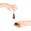 Two hands holding the Rosy Gold Nouveau Vibrating Egg and its remote control, showcasing elegance and playful control.