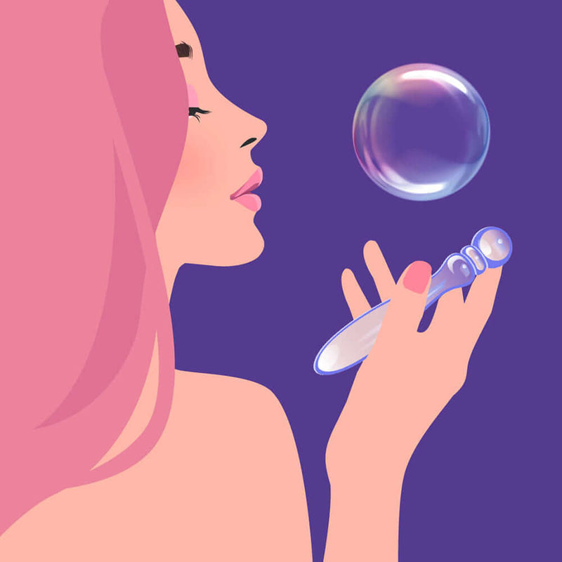 A woman with pink hair holding the Biird Cecii Beaded Glass Dildo, admiring a bubble, against a purple background.