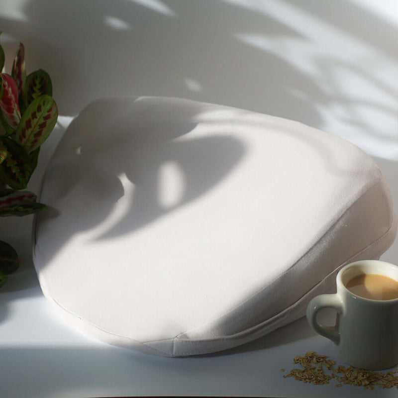 Dame Pillo Sex Pillow Oat on a table near a cup of coffee, enhancing intimacy and comfort in the bedroom.