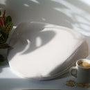 Dame Pillo Sex Pillow Oat on a tabletop with a cup of coffee and plants in the background, designed for comfort.
