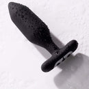 Je Joue Onyx Vibrating Butt Plug Black with water droplets on a surface, showcasing its smooth design.