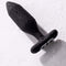 Je Joue Onyx Vibrating Butt Plug Black with water droplets on a surface, showcasing its smooth design.