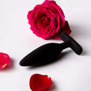 Je Joue Egon Vibrating Butt Plug Black beside rose petals and a flower, showcasing luxurious design and comfort.