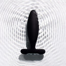 Je Joue Vesta Vibrating Butt Plug Black on textured surface with water ripples.
