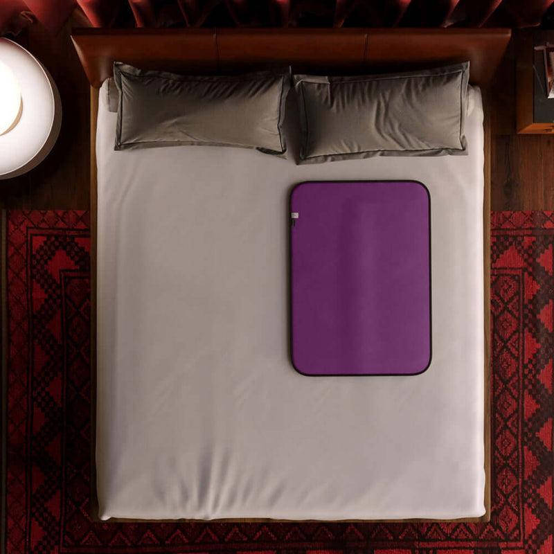 Liberator Fascinator Mini Waterproof Throw Blanket Purple on a bed with gray pillows, showcasing its sleek design for spontaneous adventures.