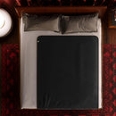 Liberator Fascinator Waterproof Throw Regular Blanket Black on a bed with decorative pillows and an area rug.