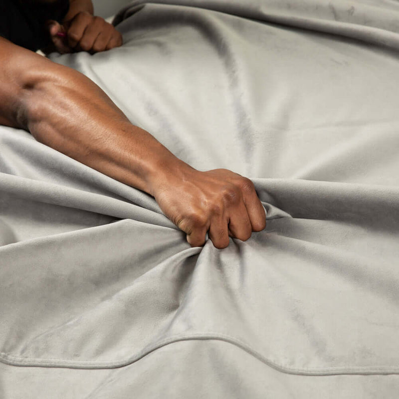 Close-up of a hand gripping the soft texture of the Liberator Fascinator Waterproof Throw Travel Blanket Gray.