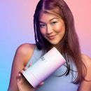 A happy woman holding a VUSH Shine G-Spot Vibrator packaging with colorful gradient background.