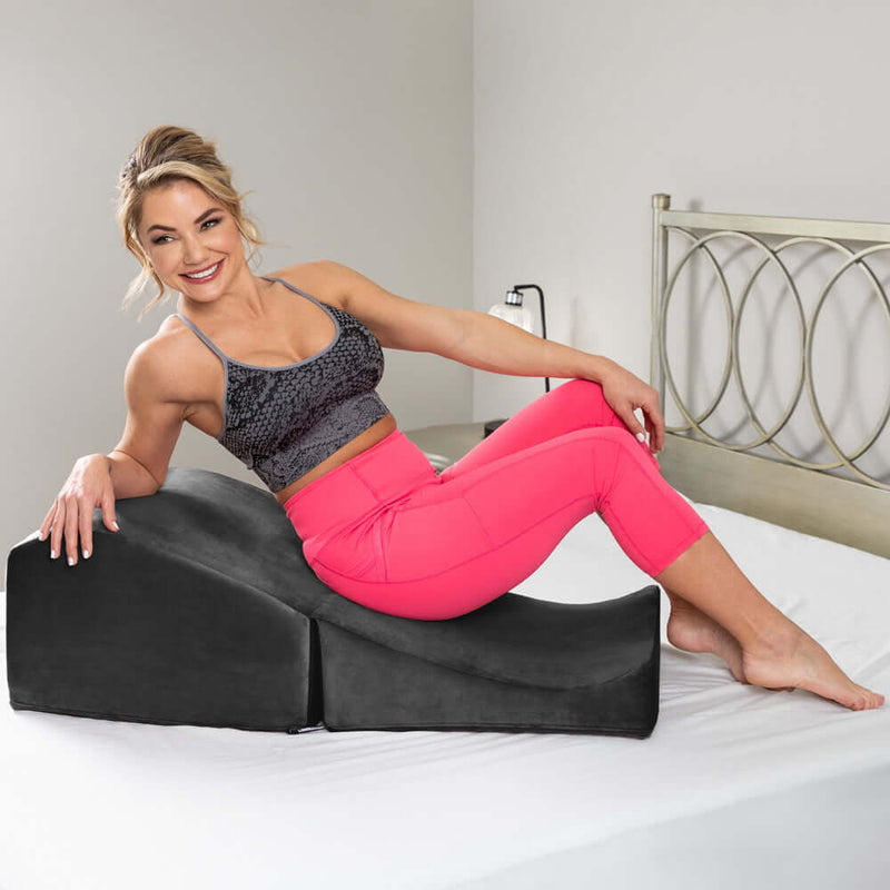 Liberator Flip Ramp Sex Positioning Pillow Black on a bed with a smiling woman in athletic wear.