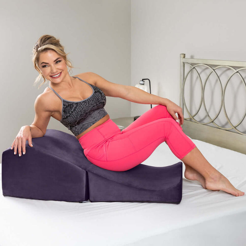 Woman using Liberator Flip Ramp Sex Positioning Pillow Plum in playful pose on bed.