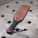 Stockroom Essentials Leather Wrapped Spanking Paddle on a textured surface showcasing its design and quality.