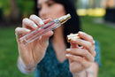 Eye Of Love Bloom Attract Him Pheromone Parfum Sunny Daze bottle held by a woman outdoors.