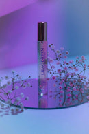 Eye Of Love Bloom Attract Him Pheromone Parfum Lilac Dream bottle with flowers on a reflective surface.