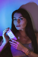 Model holding Eye Of Love Bloom Attract Him Pheromone Parfum Lilac Dream in a colorful lighting setting.