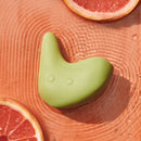 OhNut Kiwi Vibrating Personal Massager Green resting on rippled surface with orange slices around.
