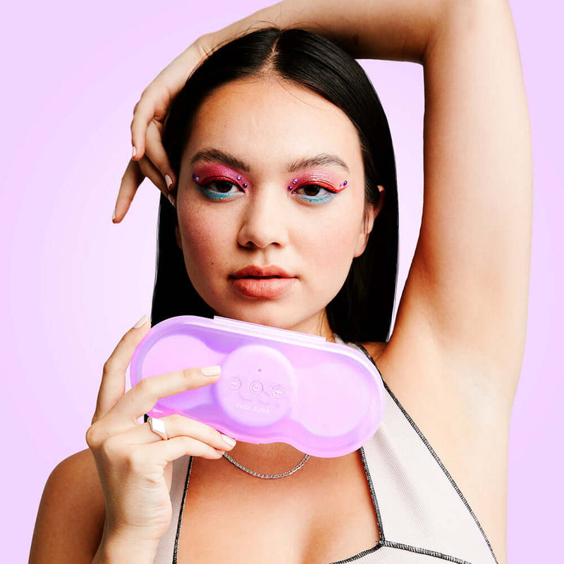 VUSH Aura Wireless Rechargable TENS Device with Travel Case held by a model with colorful eye makeup.