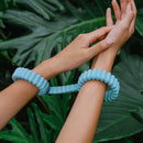 Biird Biind Silicone Cuffs Mint showcased on wrists against a backdrop of tropical foliage.