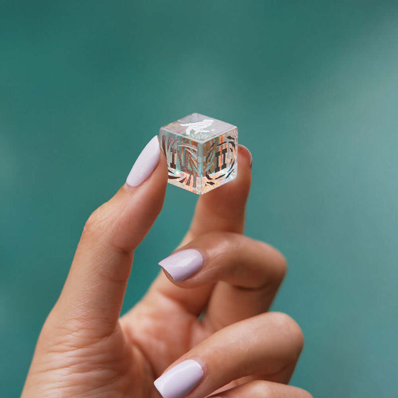 Clear decorative cube held between fingers on a teal background.