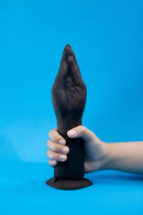 b-Vibe Vibrating Silicone Fisting Dildo held in hand against a blue background.