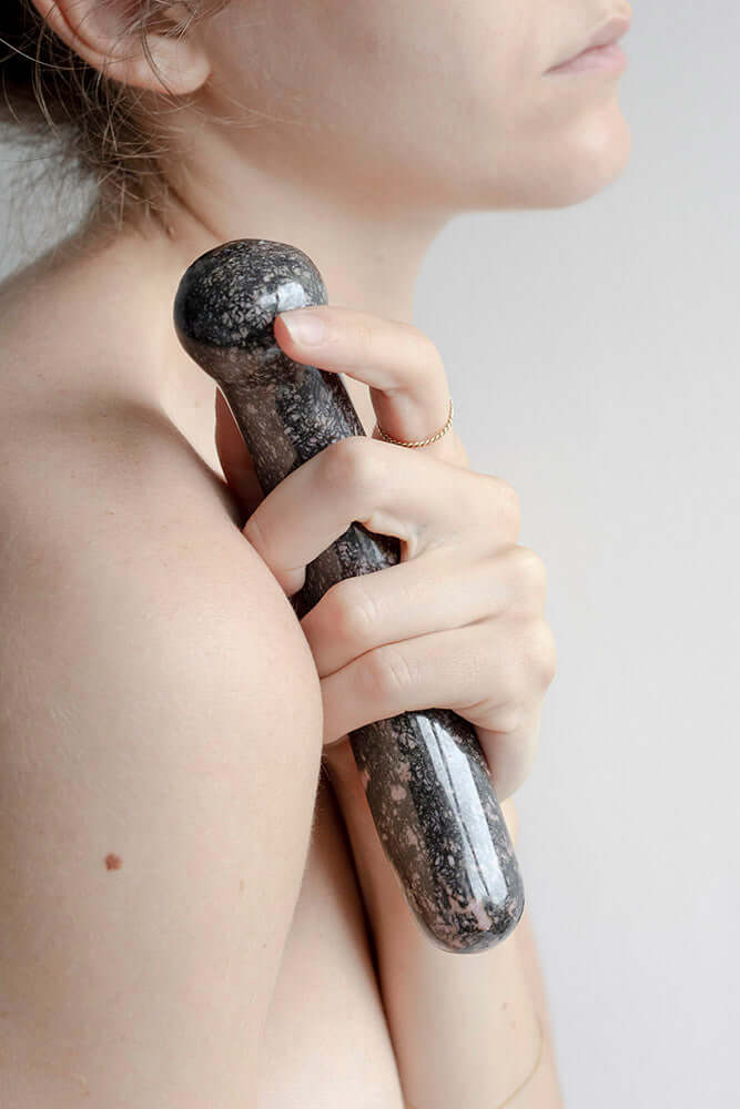 A woman holding the Chakrubs Anahata Curve Rhodonite Wand against her shoulder, showcasing its design and texture.